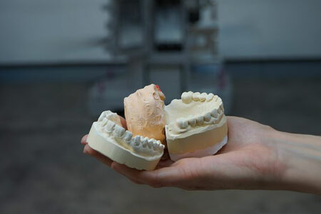 Plaster recycling with the jaw crusher type EB a hand holds old plaster casts from the dentist in front of the single-toggle crusher in the foreground
