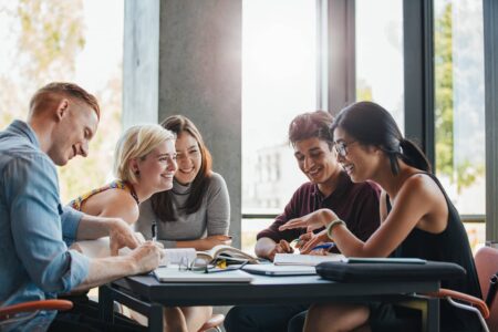Eine Gruppe Auszubildender beim gemeinsamen Lernen. 2 junge Männer und 3 junge Frauen sitzen lernend und scherzend am Tisch