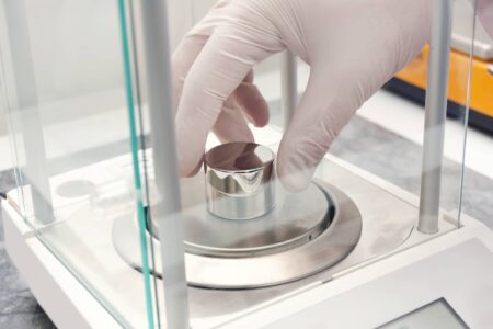 A person wearing gloves places a sample container on a laboratory balance